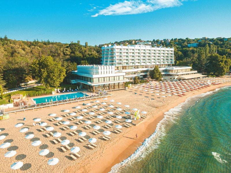 View of a beach hotel with sun loungers and umbrellas on the sandy shore next to clear sea.