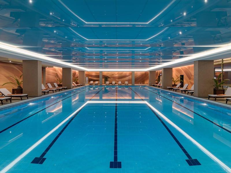 Interior of a modern indoor pool with blue lanes and comfortable lounge chairs.