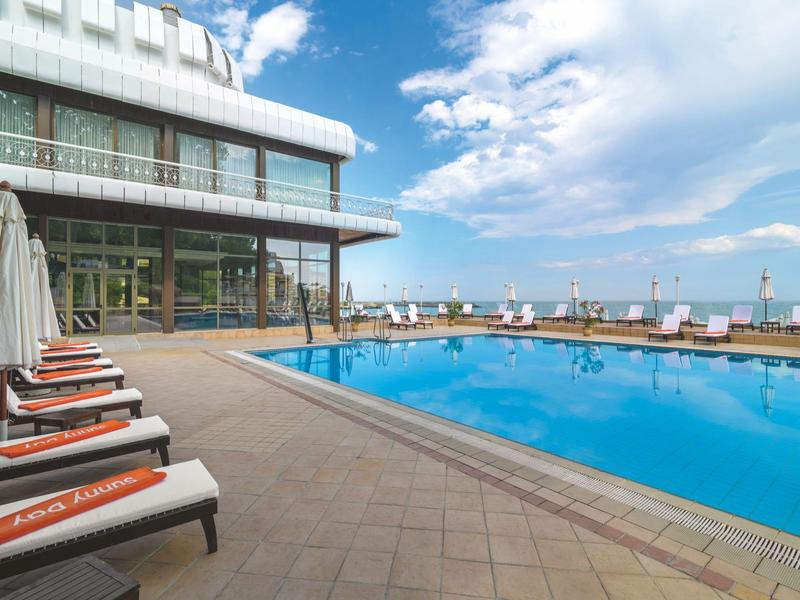 Outdoor pool with lounge chairs and sky view in front of a hotel building