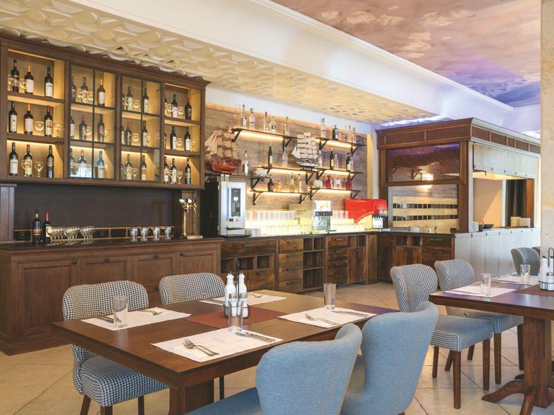 Elegant restaurant area with wooden furniture, chairs, and a wall of shelves filled with bottles.