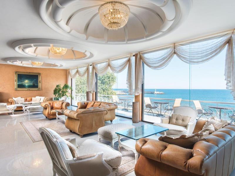 Bright hotel lounge with large windows, sea view, and elegant furnishings.
