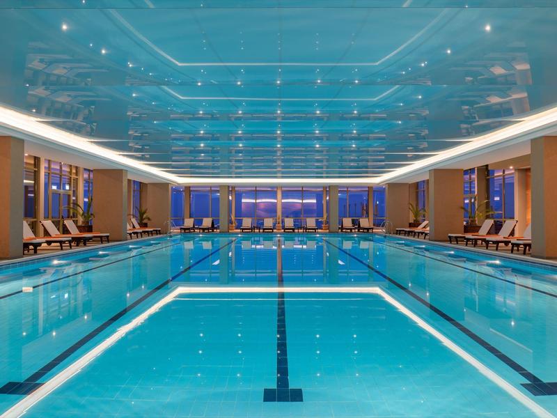 Indoor swimming pool with blue ceiling and lounge chairs on both sides.