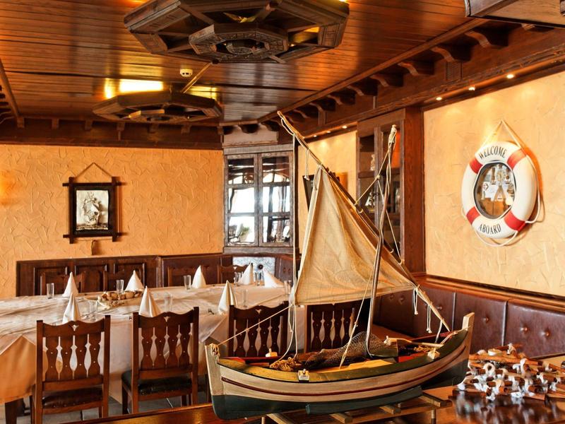Cozy restaurant area with wooden furniture, nautical decor, and model sailboat