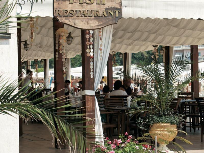 Outdoor covered restaurant area with plants and wooden sign.