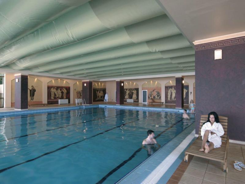 Indoor pool with two people, one swimming and one sitting on a bench