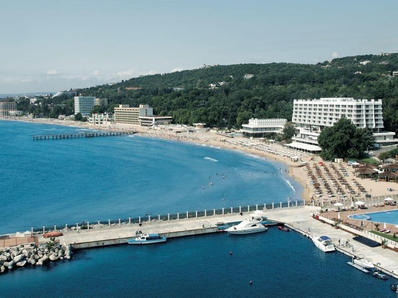 Beach hotel along the shore with a long pier and sun loungers on the sandy beach.