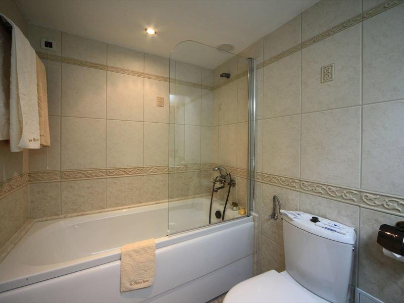 Modern bathroom with bathtub, shower screen, towels, and toilet.