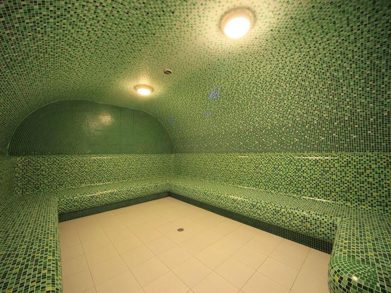 Lit steam room with green mosaic tiles and rounded walls.