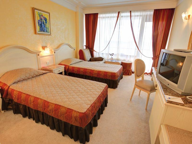 Hotel room with two single beds, yellow walls, and large windows with red curtains.