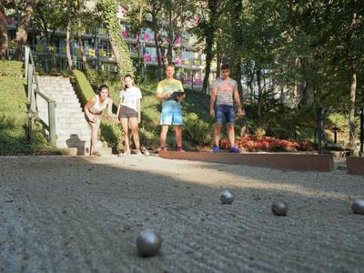 Vier mensen spelen petanque op een schaduwrijke buitenbaan met grind