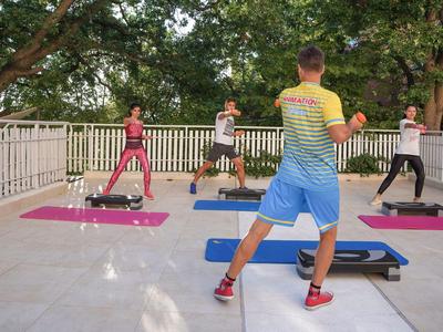 Groep traint op yogamatten met steppers buiten op een terras.