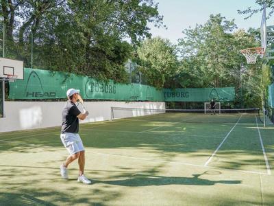 Een man speelt op een buiten tennisbaan omringd door bomen.