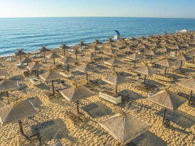 Strand mit vielen Sonnenschirmen aus Stroh und einem weiten Blick auf das ruhige blaue Meer.