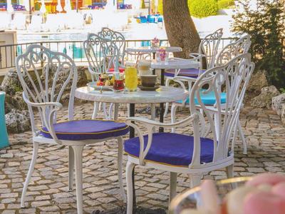 Café en plein air avec chaises et tables en métal blanc sur un sol pavé par temps ensoleillé.