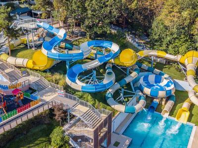 Veduta di un parco acquatico con più scivoli d'acqua blu e gialli accanto a una piscina in un resort alberghiero.