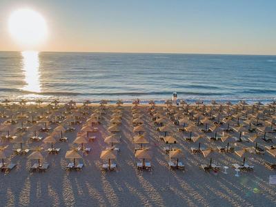Spiaggia con numerosi ombrelloni e lettini all'alba sul mare calmo.