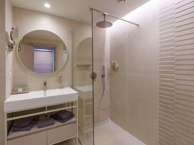 Bagno moderno in hotel con parete doccia in vetro, specchio rotondo e lavabo bianco.
