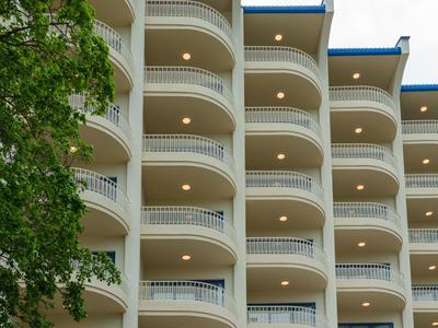 Hotel su più piani con balconi curvi e facciata gialla accanto a un gruppo di alberi verdi.