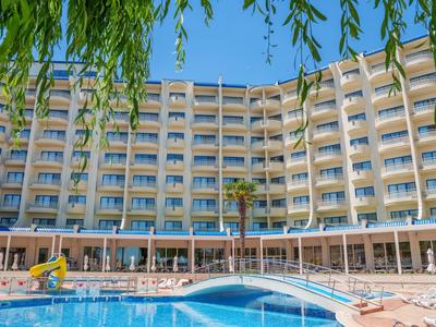 Grande hotel con piscina, ombrelloni e cielo azzurro sullo sfondo.