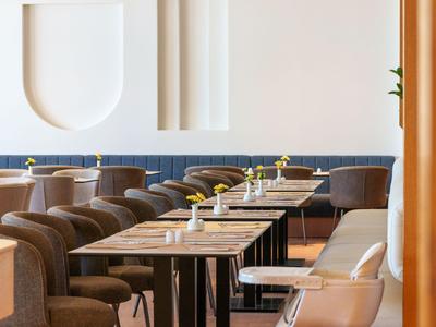 Area ristorante moderna dell'hotel con sedie marroni, tavoli in legno e arte murale minimalista.