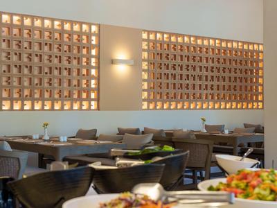 Sala da pranzo di hotel moderna con tavoli e sedie in legno e illuminazione decorativa.