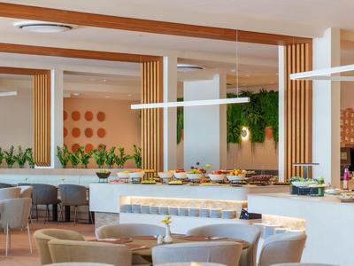 Area ristorante moderna dell'hotel con tavoli, sedie e un buffet con cibo.
