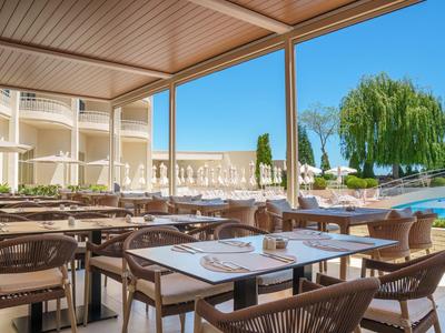 Terrazza coperta con tavoli apparecchiati con vista sulla piscina e il giardino di un hotel.