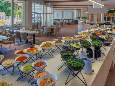 Buffet con varie insalate e contorni in un ristorante d'hotel luminoso con grandi finestre.