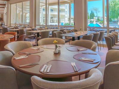 Ristorante elegante con tavolo rotondo in legno e sedie comode vicino a grandi finestre con vista piscina.