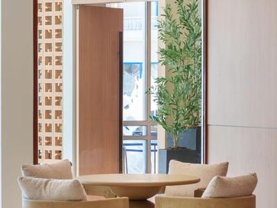 Area lounge moderna dell'hotel con tavoli rotondi in legno e sedie imbottite accanto a grandi finestre.