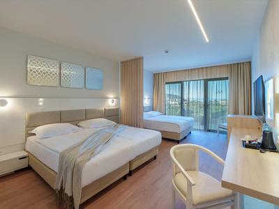 Modern hotel room with two beds, balcony, and view of green landscape.
