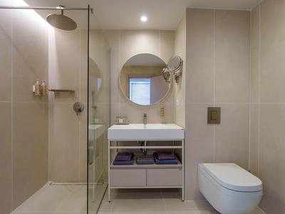 Modern hotel bathroom with walk-in shower, round mirror, and wall-mounted toilet.