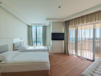 Bright hotel room with two beds, balcony, and floor-to-ceiling windows with curtains.