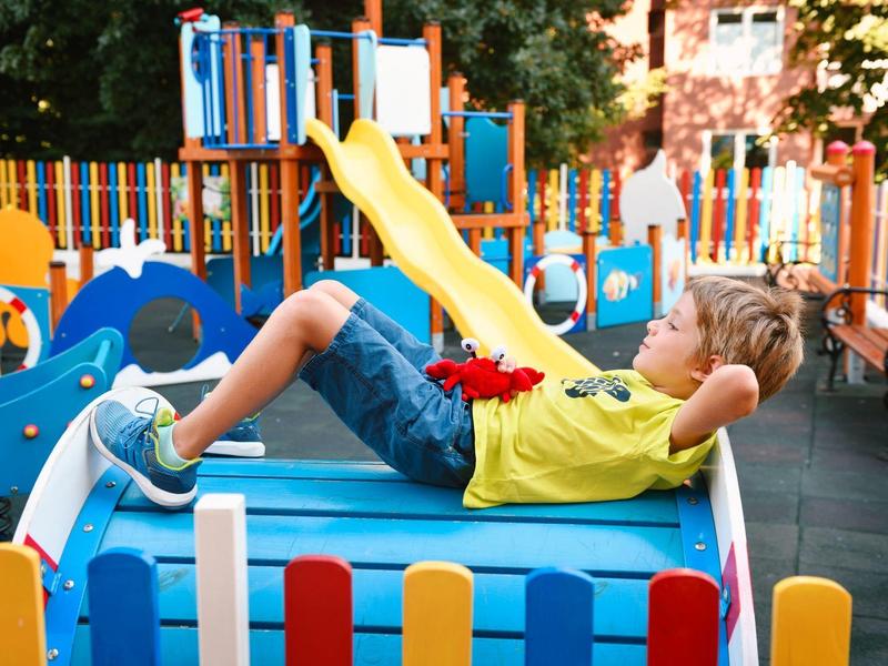 Un enfant est allongé détendu sur une structure de jeu bleue entourée de clôtures colorées et d'équipements de jeu.