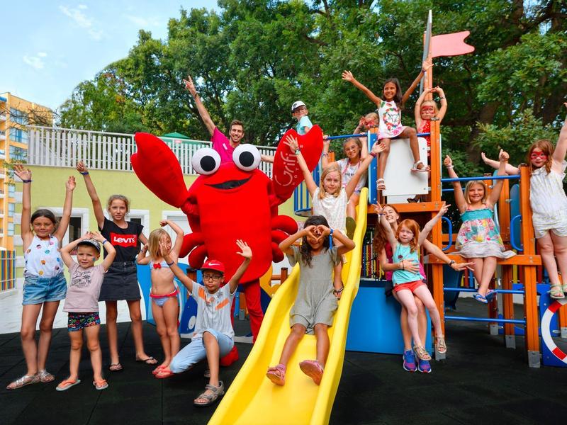 Des enfants jouent sur une aire de jeux colorée avec toboggan et mascotte homard.