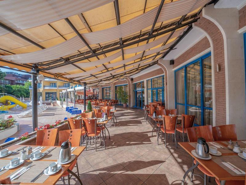 Terrasse extérieure couverte d'un restaurant avec de nombreuses tables et chaises à côté d'un hôtel.