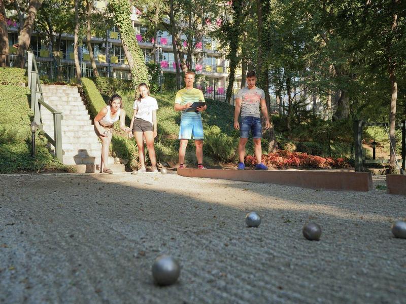 Quatre personnes jouent à la pétanque sur un terrain sablonneux en plein air par une journée ensoleillée.
