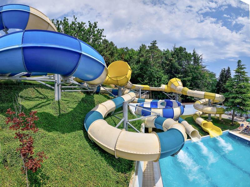 Plusieurs toboggans aquatiques colorés aboutissent dans une grande piscine entourée de verdure.