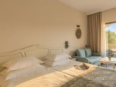 Lichte hotelkamer met tweepersoonsbed, banken en balkon met uitzicht naar buiten.