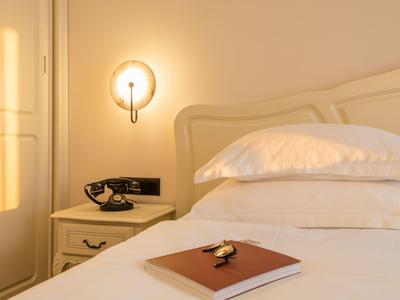 Gezellige hotelkamer met wit bed, nachtkastje, telefoon en wandlamp bij warm licht.