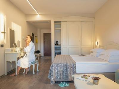 Lichte hotelkamer met bed, zithoek en vrouw in badjas bij kaptafel