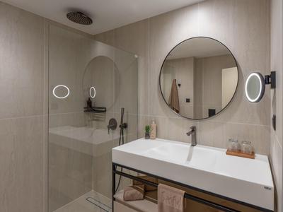 Moderne badkamer met ronde spiegel, glazen douche en grote wastafel op een donker metalen frame.