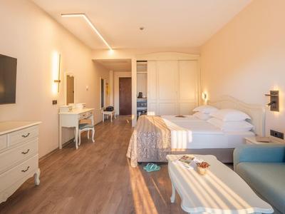 Licht hotelkamer met tweepersoonsbed, tv, bureau en zithoek met bank en tafel.