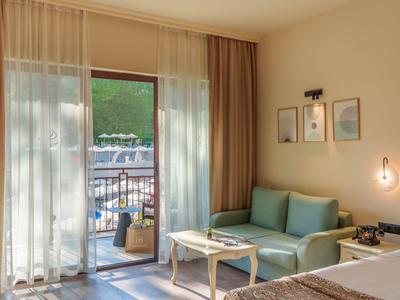 Helle Hotelzimmer mit Couch, Tisch und Blick auf einen Balkon mit Bergkulisse.