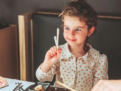 Ein Mädchen sitzt am Tisch mit Essstäbchen und speist asiatische Gerichte.