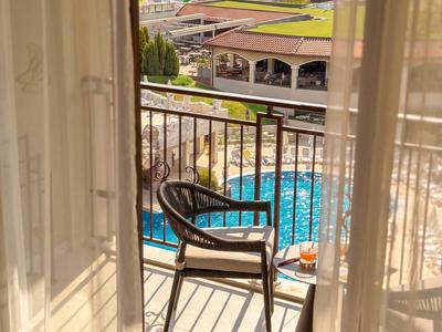 Blick durch Gardinen auf Balkon mit Stuhl, Tisch und Pool im Hotelresort.