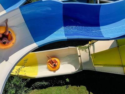 Zwei Personen fahren auf orangenen Reifen eine blaue Wasserrutsche im Freien hinab.