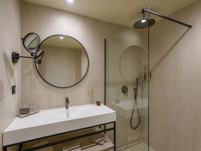 Modernes, helles Badezimmer mit rundem Spiegel und begehbarer Dusche in neutralen Tönen.