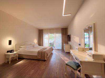 Helles Hotelzimmer mit Doppelbett, Holzboden, Schreibtisch und Balkon mit Vorhängen.