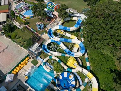 Wasserpark mit mehreren blauen und weißen Wasserrutschen, umgeben von Grünflächen und Gebäuden.